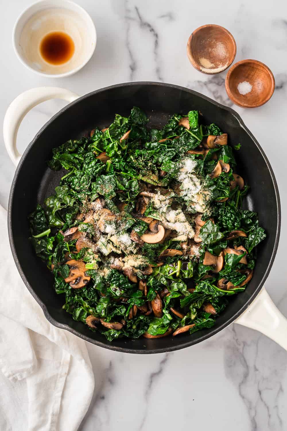 Spices added to kale and mushrooms in sklilet.