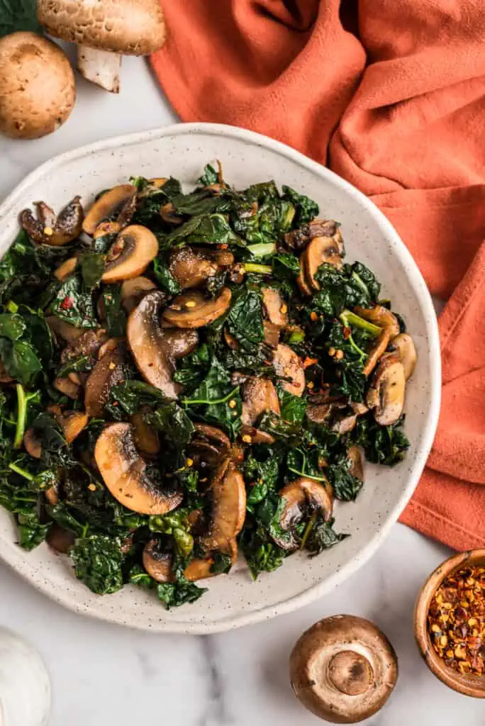 Balsamic kale and mushrooms in a white bowl, orange napkin on the side.