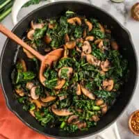 Wood spoon in a large skillet filled with balsamic kale and mushrooms.