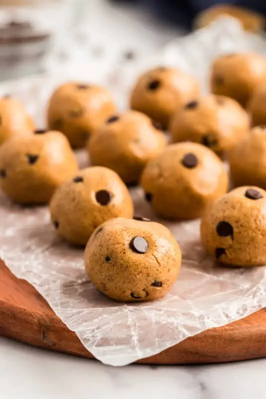 Chocolate chip almond butter energy balls lined up on a wood cutting board.