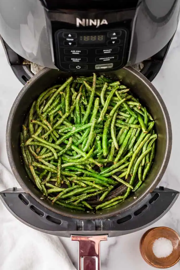 Frozen green beans in air fryer basket after shaking the basket. 