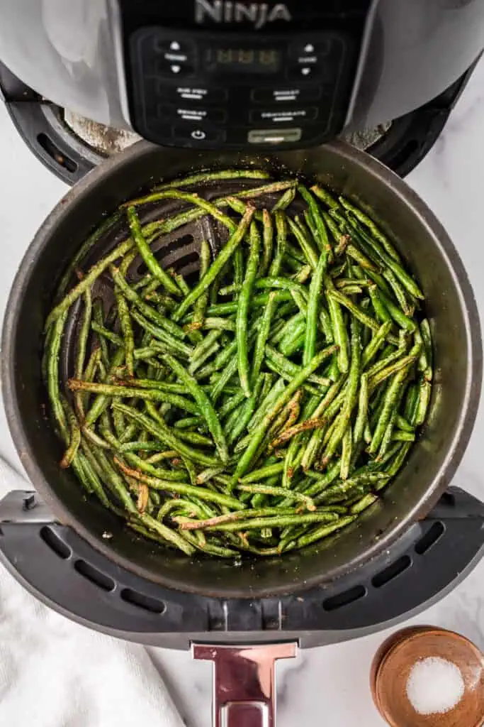 Crunchy frozen green beans in air fryer basket after cooking. 