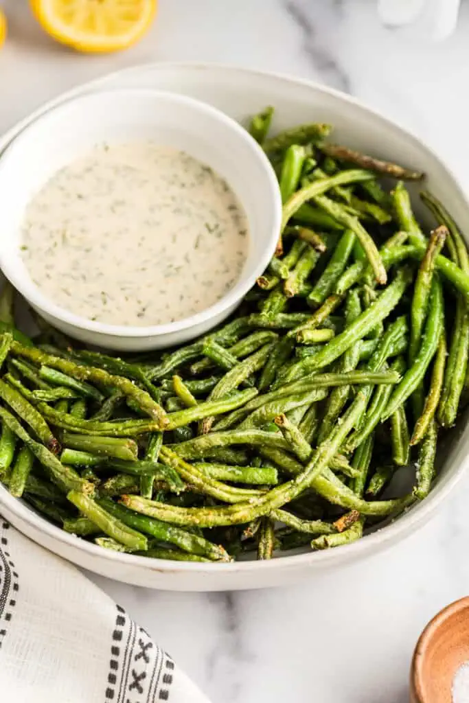 Air fried frozen green beans on a white plate, lemon tahini dip on the side.