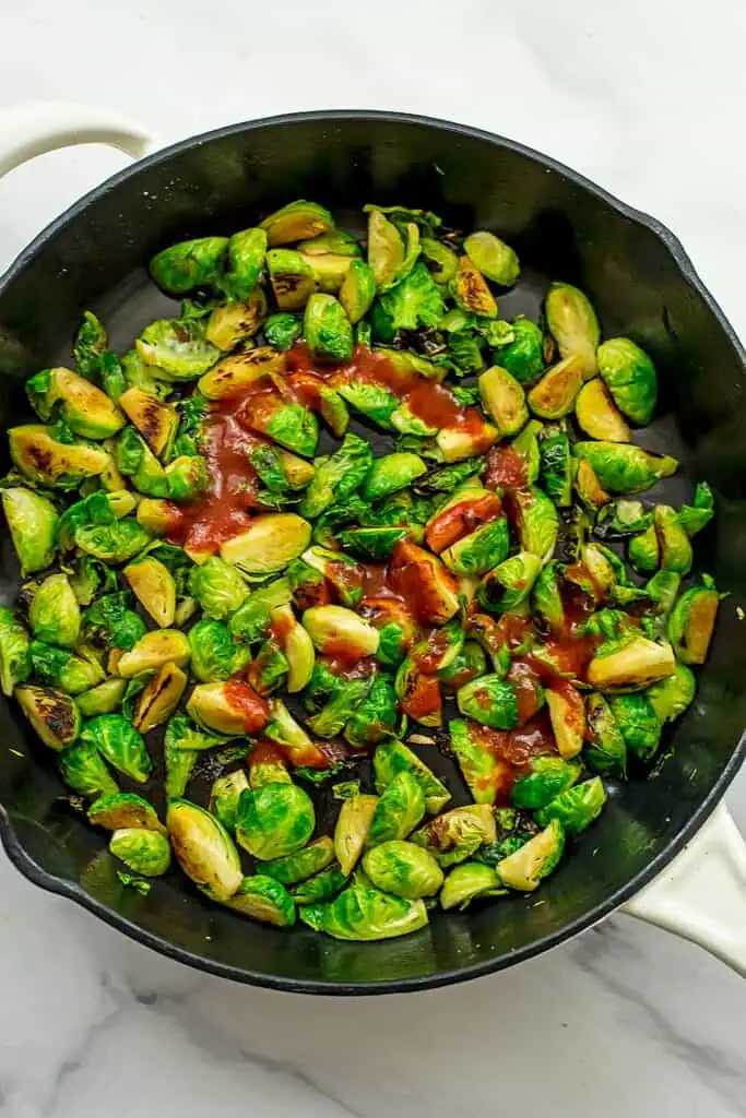 Sriracha added to brussel sprouts in skillet.