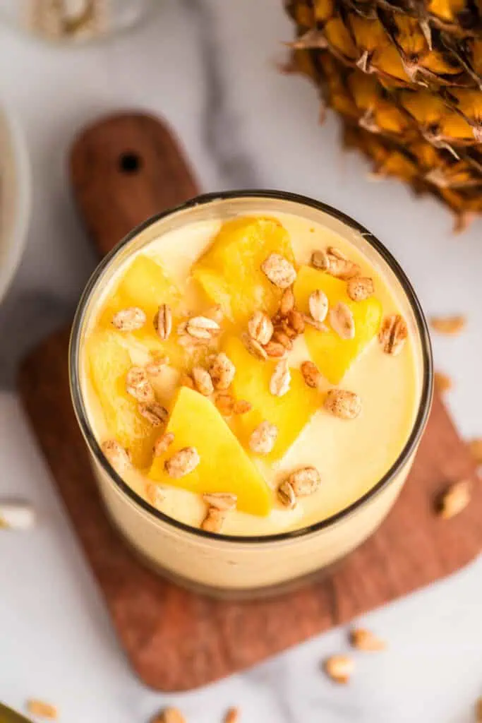 Chopped fruit on top of a mango pineapple smoothie in a glass.