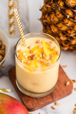 Pineapple mango smoothie with straw in glass with pineapple in background.