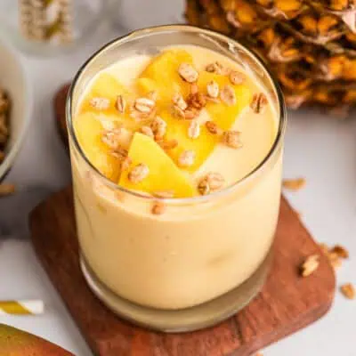 Pineapple mango smoothie in a glass on a wood board.