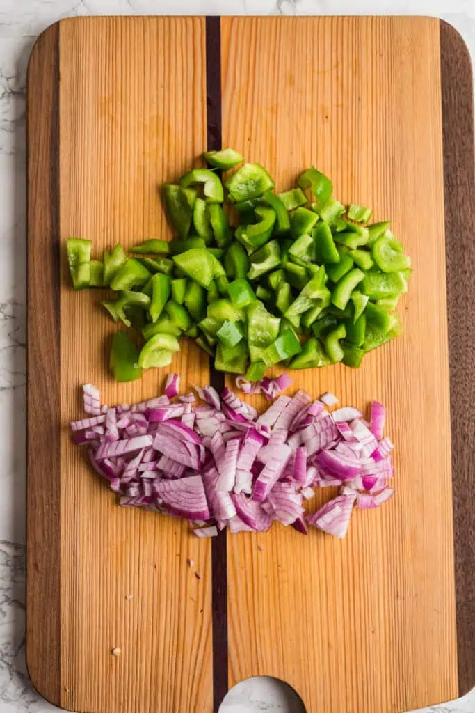 Chopped green bell pepper and red onion on cutting board.