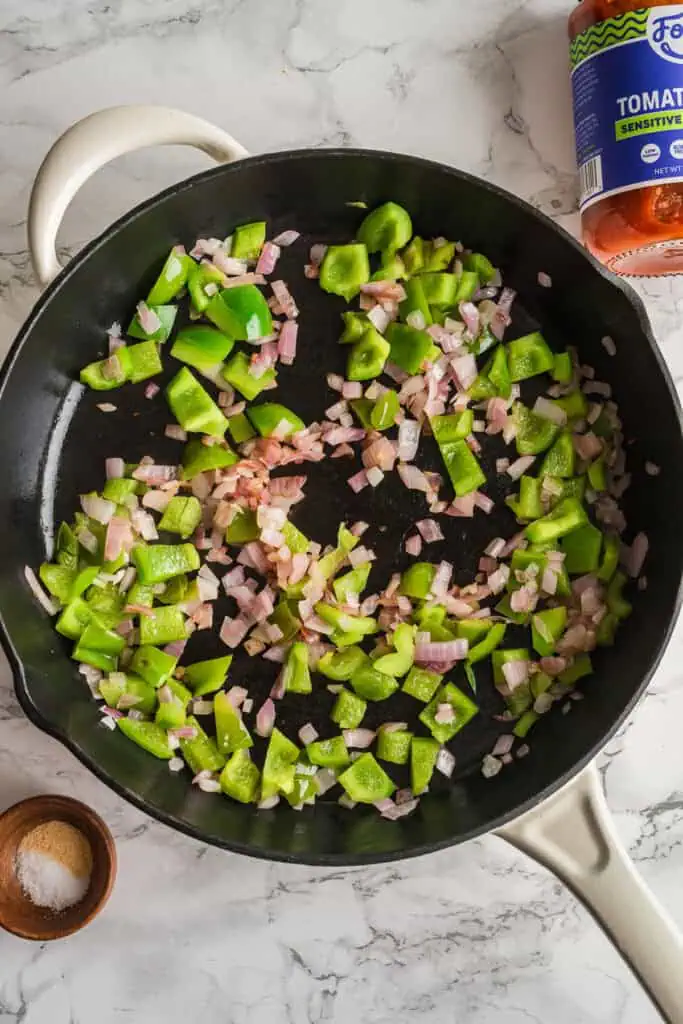 Green pepper and red onion cooking in cast iron skillet.