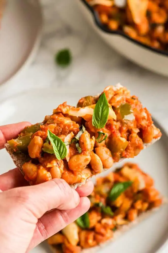 Hand holding flat bread cracker with pizza beans on top.
