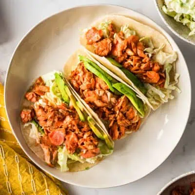 White plate filled with three bbq salmon tacos stacked against each other.