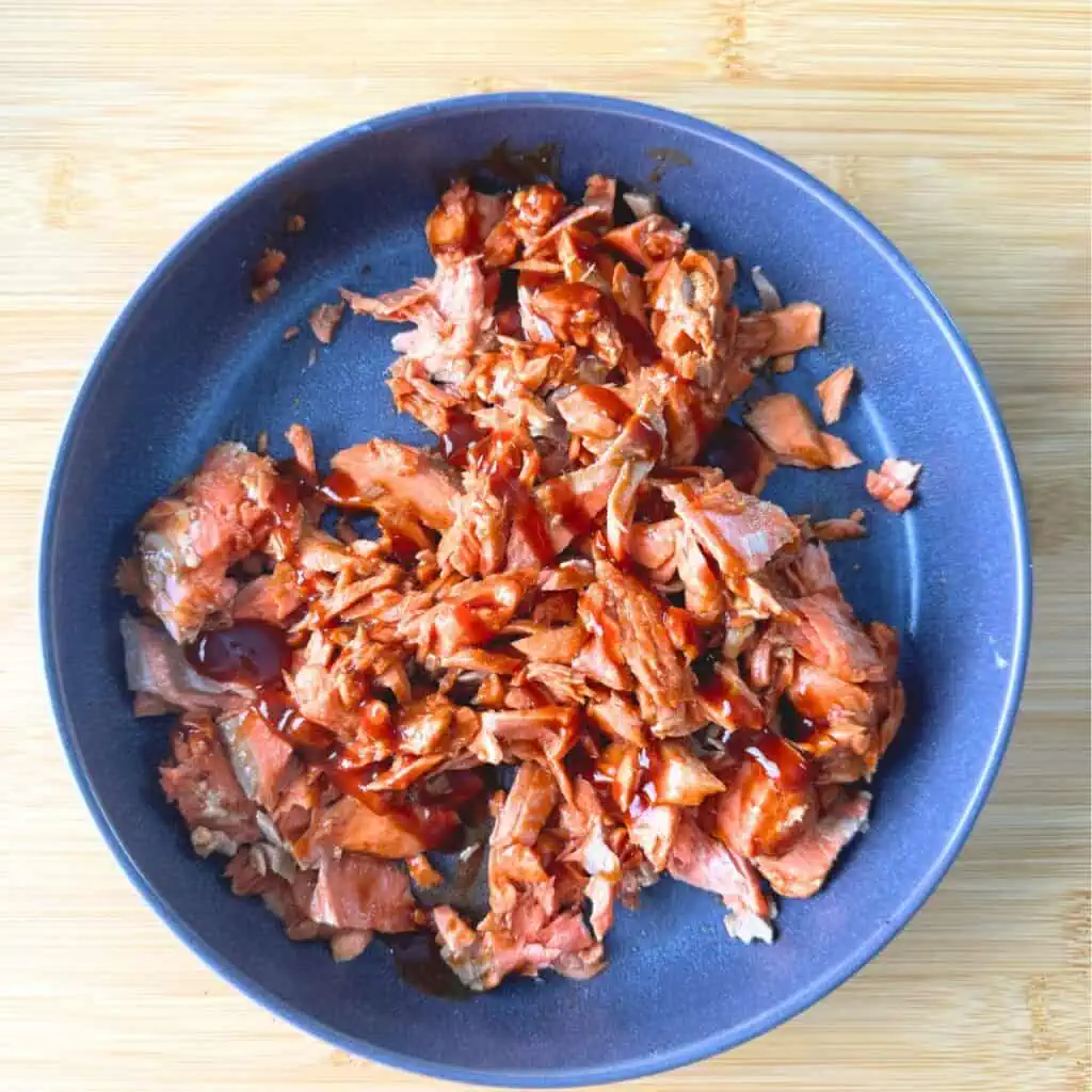 Salmon flaked in a blue bowl, bbq sauce poured over the top.