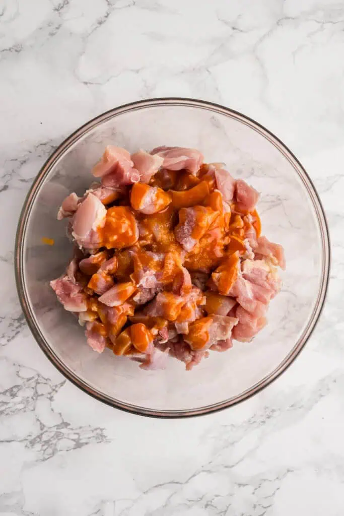 Buffalo sauce poured over chicken in a glass bowl.