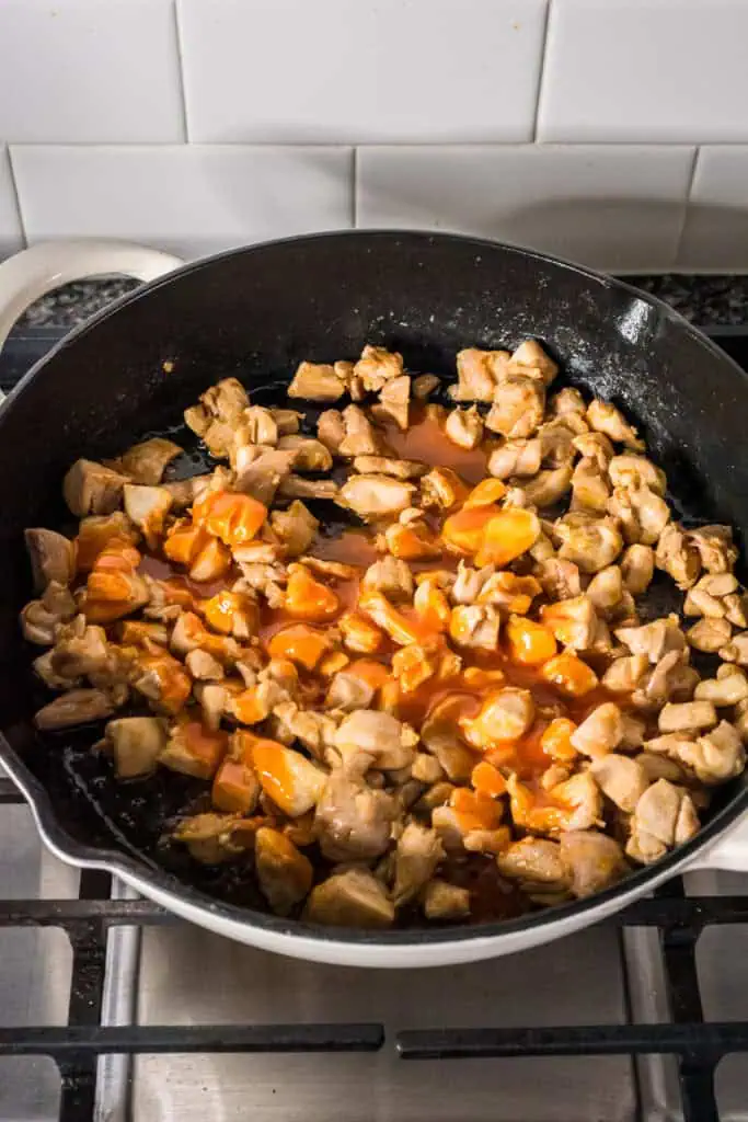 Buffalo sauce poured over chicken in a skillet.