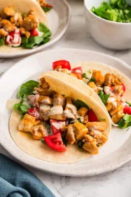 Soft shelled buffalo chicken tacos with ranch dressing on a white plate. Blue napkin on the side.