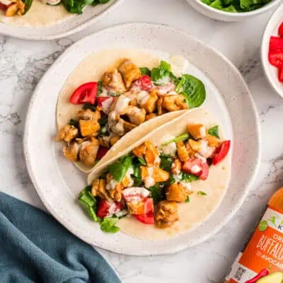 Two buffalo chicken tacos on a white plate with a blue napkin on the side.