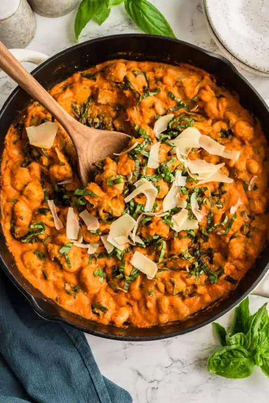 Wood spoon lifting gnocchi from the skillet of gnocchi with tomato sauce.