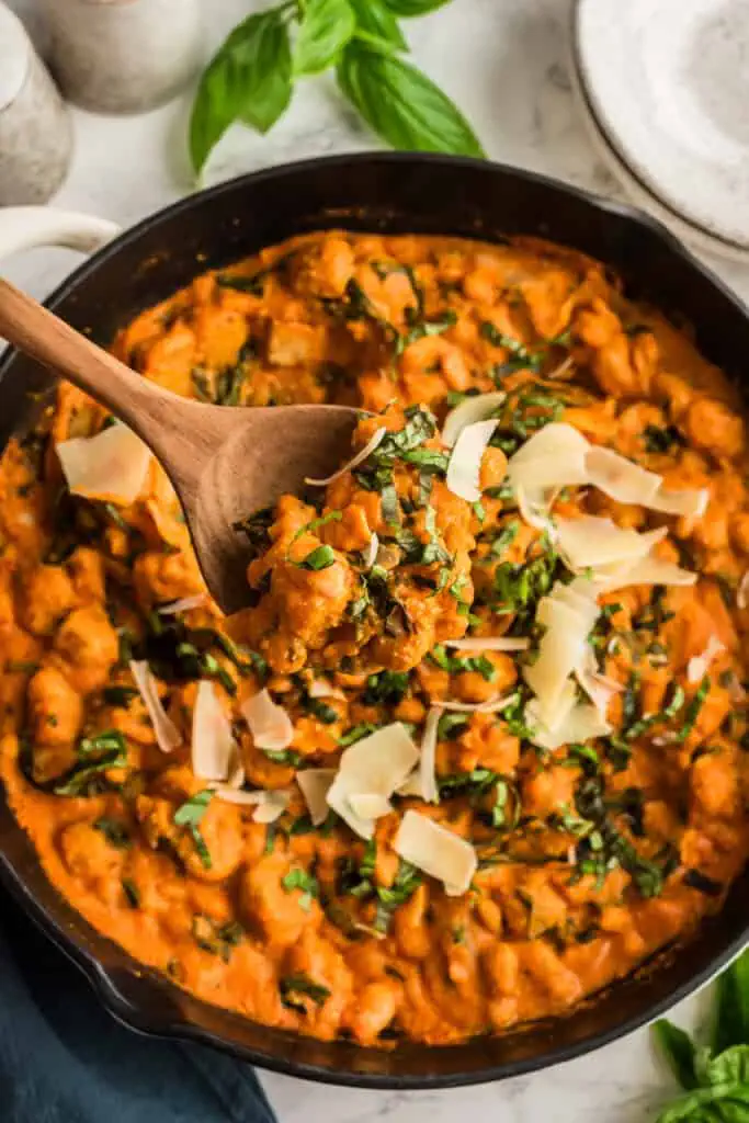 Creamy tomato gnocchi in a skillet with a wood spoon resting in the skillet.