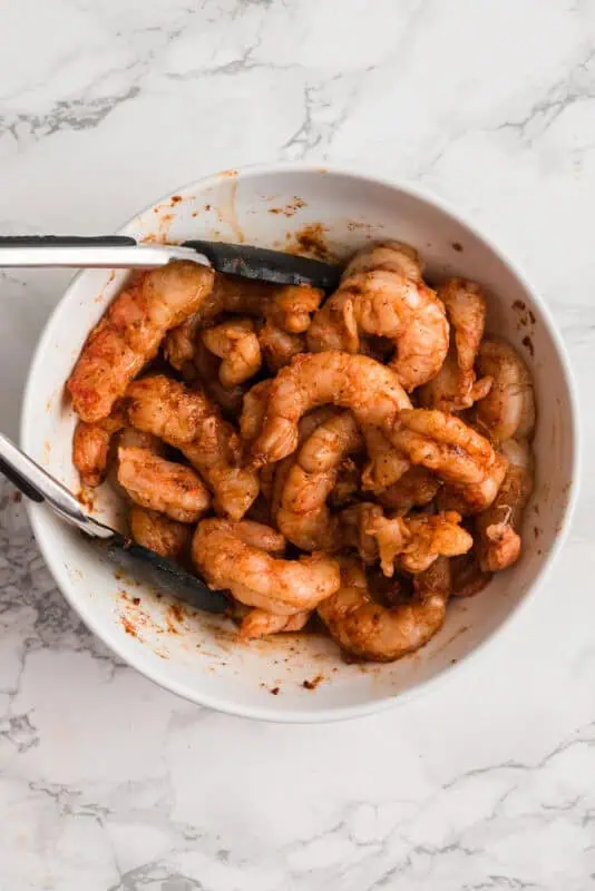 Tongs resting in bowl with blackened shrimp after tossing.