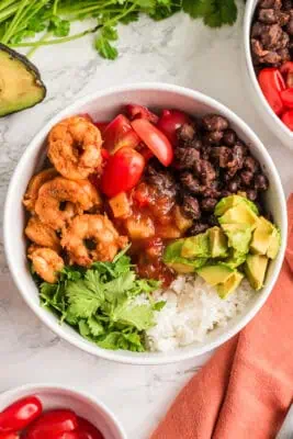 Blackened shrimp rice bowl with avocado, tomatoes, and black beans. Orange napkin on the side.