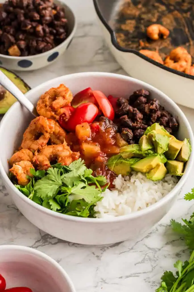 Fork resting in blackened shrimp bowl with black beans, tomato, avocado and cilantro.