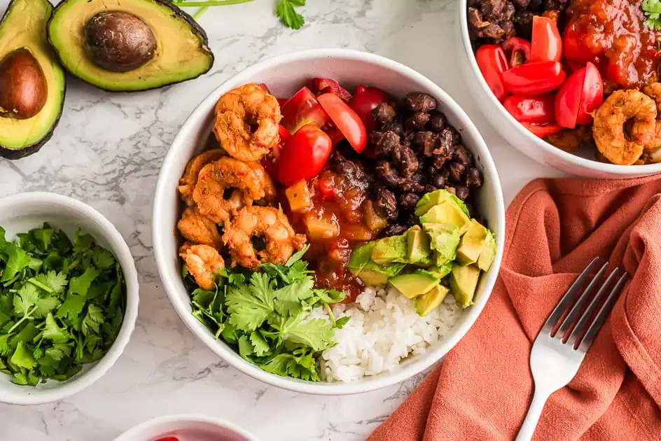 Blackened shrimp and rice in a bowl with avocado and orange napkin on the sides.