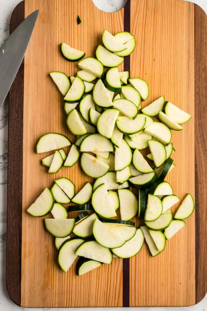 Zucchini sliced into thin moon shapes on a cutting board.