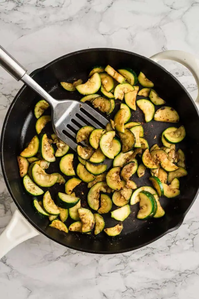 Sauteed zucchini in a cast iron skillet with spatula resting in the pan.