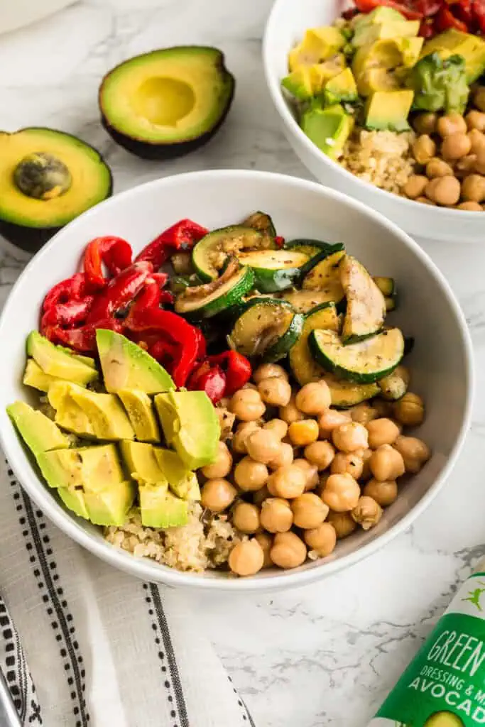 Green Goddess Bowl topped with avocado, chickpeas and zucchini in a white bowl, avocado in the background.