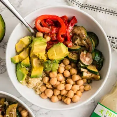 White bowl filled with avocado, chickpeas, zucchini, quinoa and roasted red peppers.