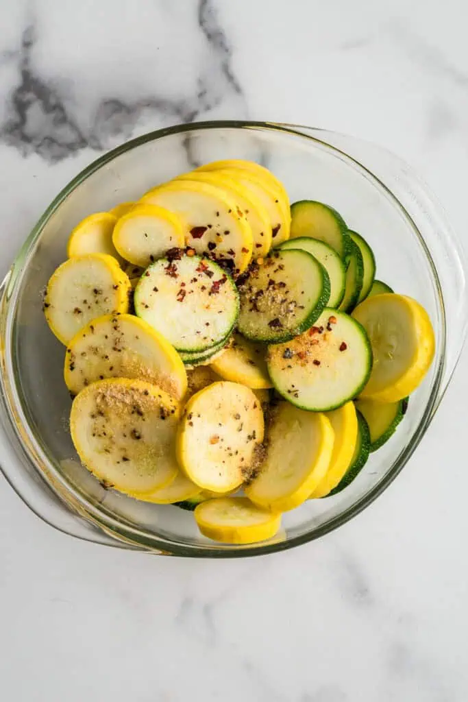 Sliced squash with spices and italian dressing in glass bowl.