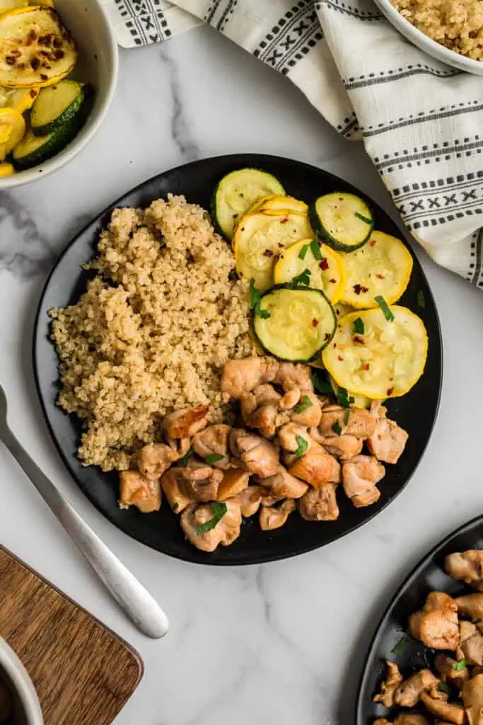 Italian chicken with sliced squash and quinoa on a black plate with fork on the side.