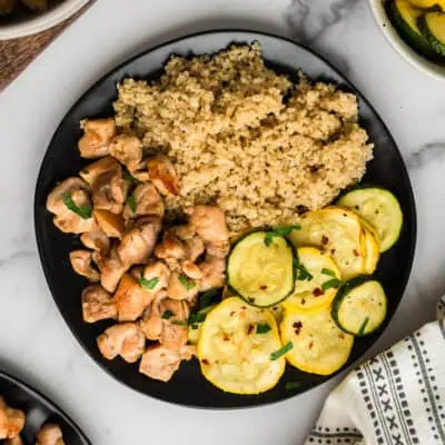 Italian chicken and veggies on black plate with quinoa.