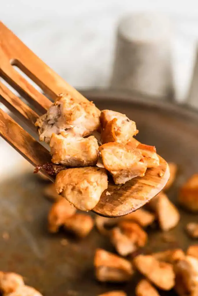 Greek chicken bites being picked up out of the pan with a wood spatula.