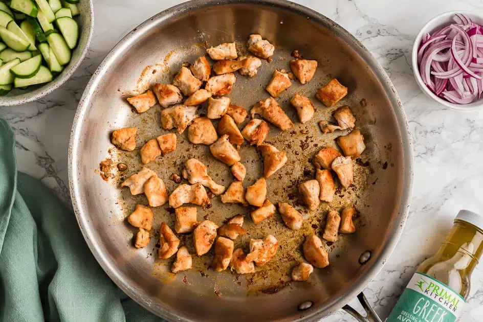 Skillet filled with greek chicken cubes, greek dressing on the side.