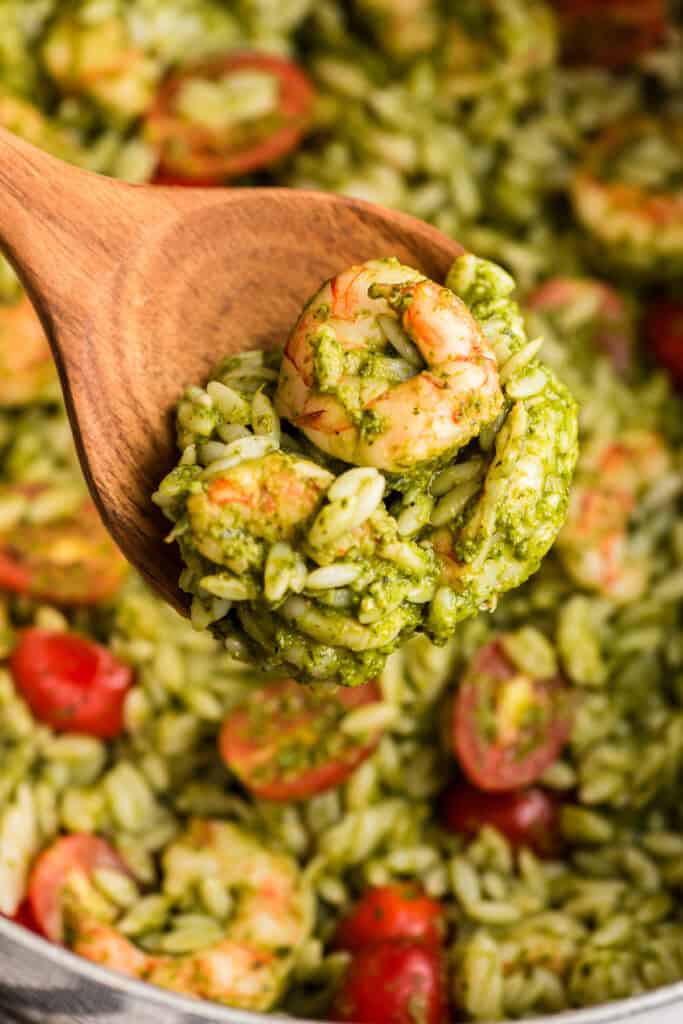 Orzo shrimp pesto being spooned out of a pot by a large wood spoon.