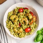 Bowl filled with shrimp pesto orzo, grey striped napkin on the side.