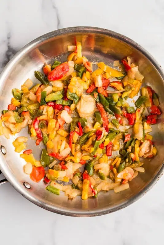 Stainless steel pan filled with frozen bell peppers and onions.