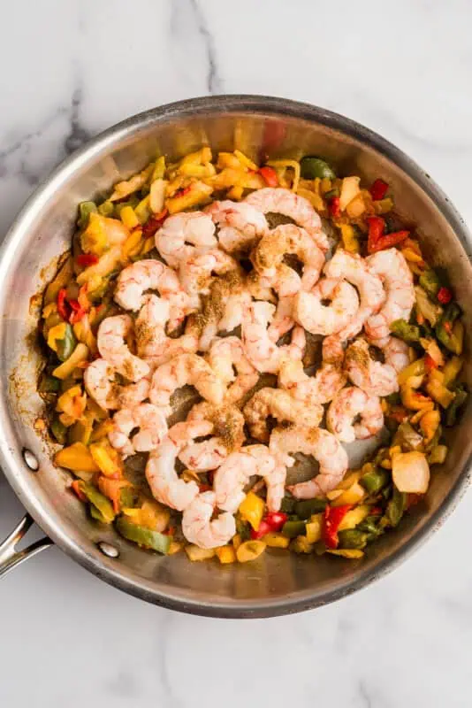 Shrimp added to a pan with peppers and onions.