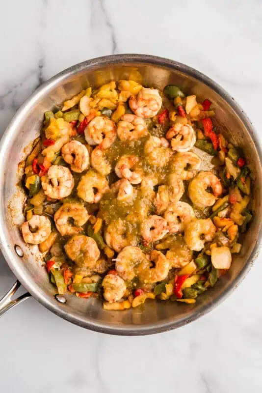 Cooked shrimp and veggies with salsa verde over top in a pan.