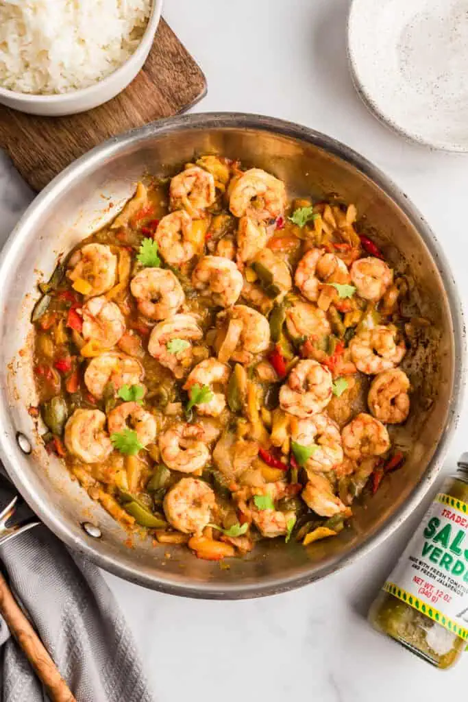 Salsa verde shrimp and veggies in a stainless steel pan with jar of salsa on the sidse.