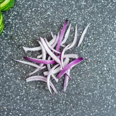 Thinly sliced red onion on cutting board.