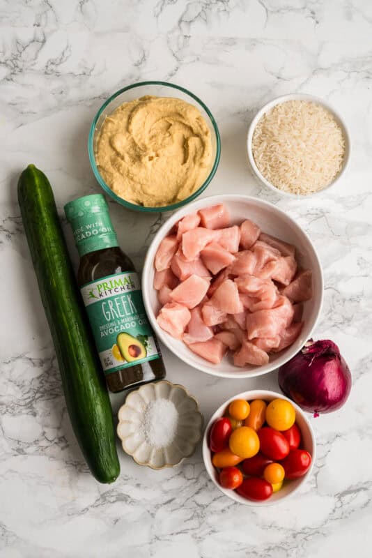 Ingredients to make Mediterranean chicken bowls on a marble countertop.