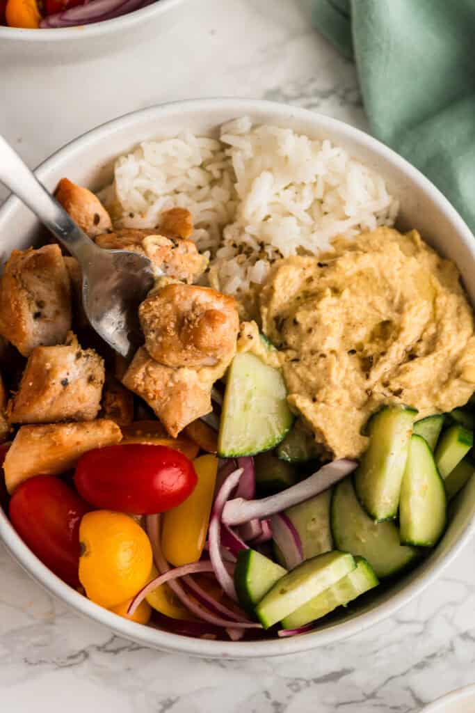 Fork resting in a bowl of Greek Chicken and Rice on a marble countertop.
