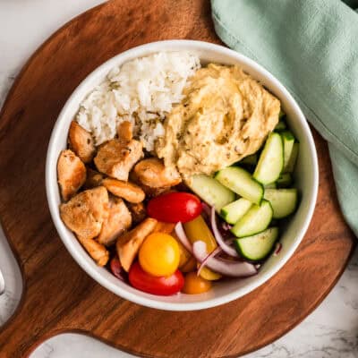 Bowl of Greek Chicken and Rice over a wooden tray with a green napkin.