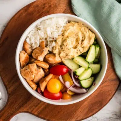 Bowl of Greek Chicken and Rice over a wooden tray with a green napkin.