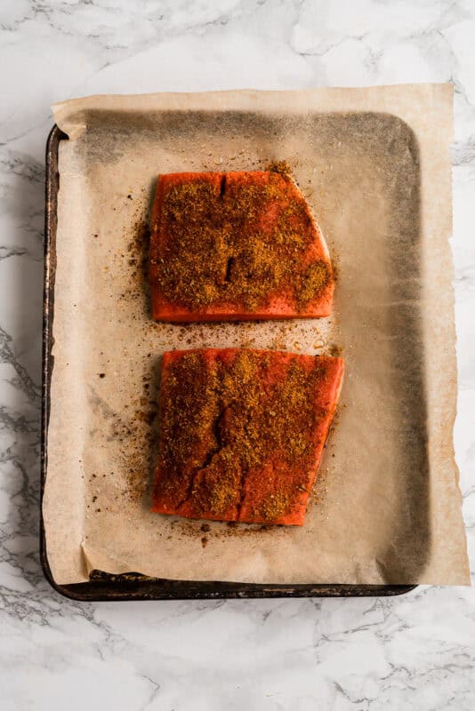 Two pieces of salmon coated in chipotle taco seasoning before cooking.