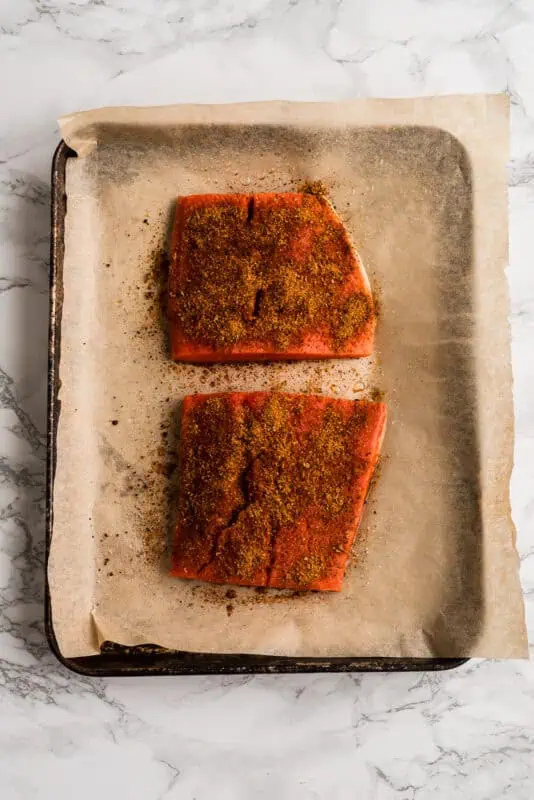 Two pieces of salmon coated in chipotle taco seasoning before cooking.