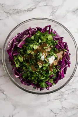 Shredded red cabbage, cilantro and spices in a glass bowl.