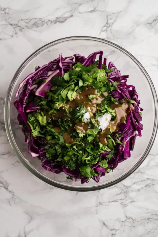 Shredded red cabbage, cilantro and spices in a glass bowl.